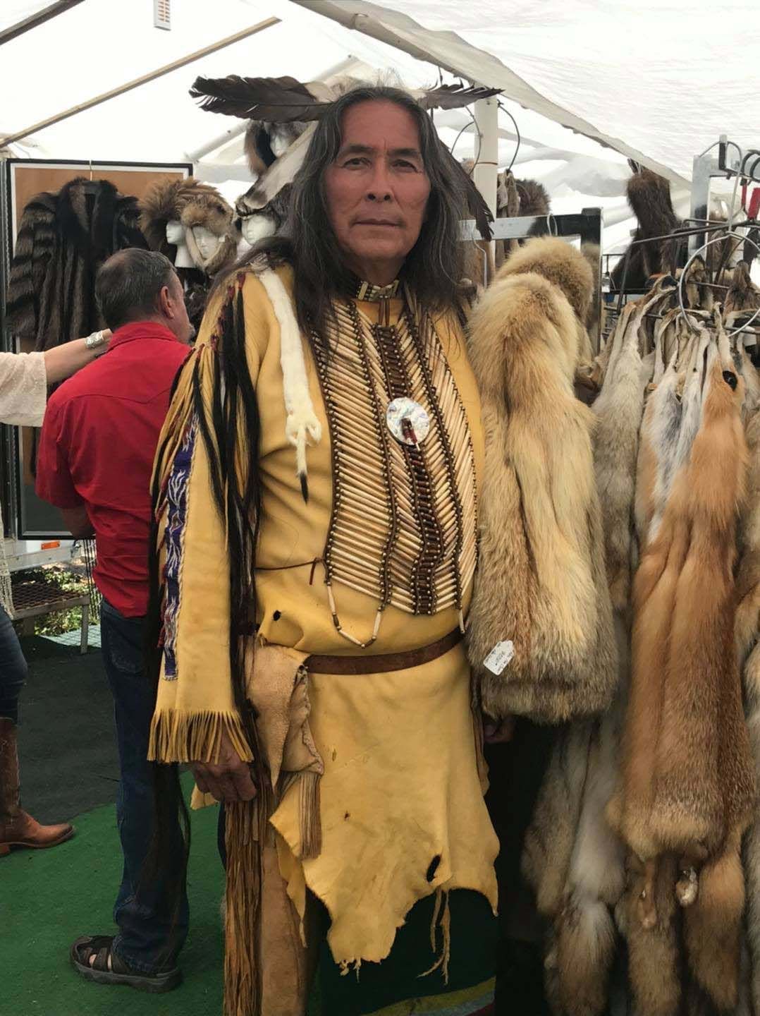 A man in a native american outfit is standing in front of furs