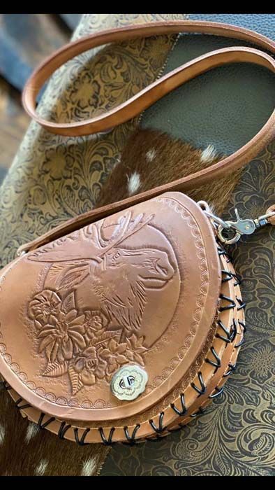 A brown leather purse with a deer on it is sitting on a table.