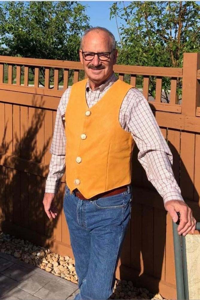 A man wearing a yellow vest is standing in front of a wooden fence.