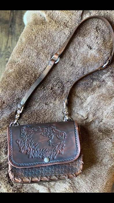 A brown leather purse with a strap is sitting on top of a piece of fur.