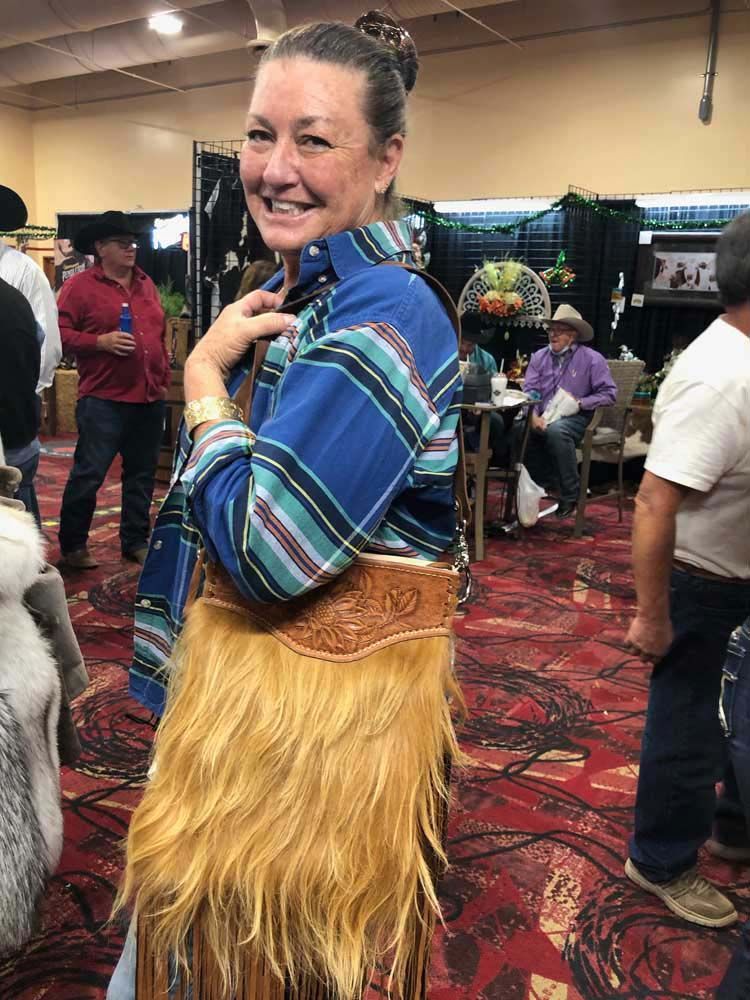 A woman is standing in a room holding a purse with fringe.