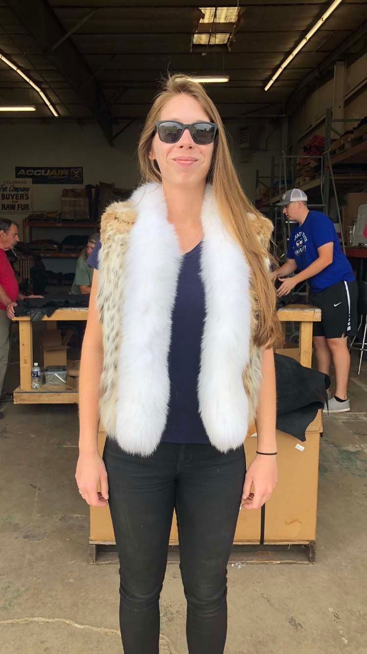 A woman wearing sunglasses and a white fur vest is standing in a warehouse.