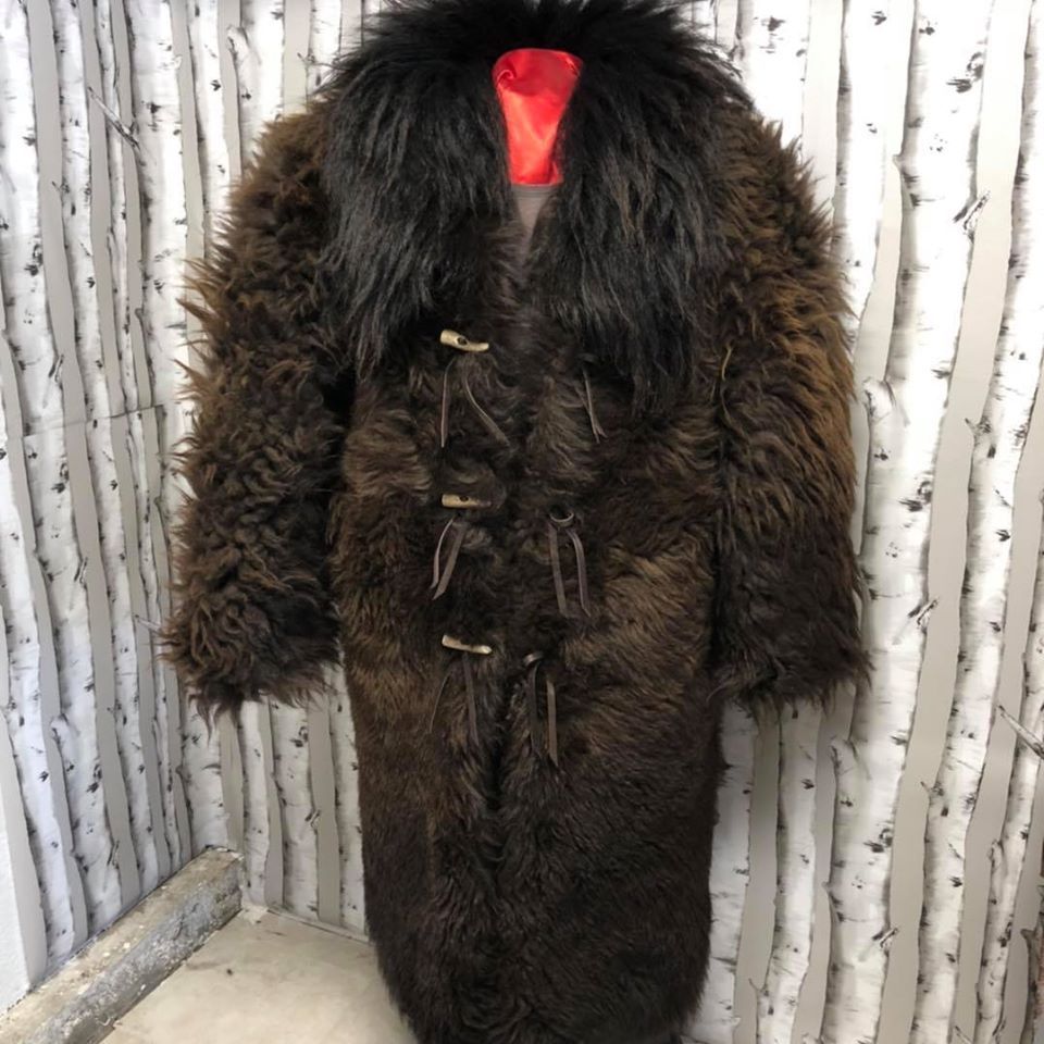A brown fur coat with a black collar is hanging on a mannequin.