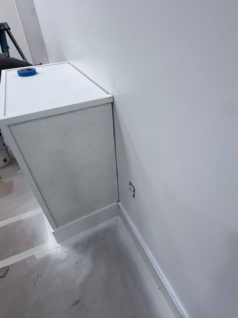 White cabinet beside a gray wall in a small utility room, with a blue object on top.