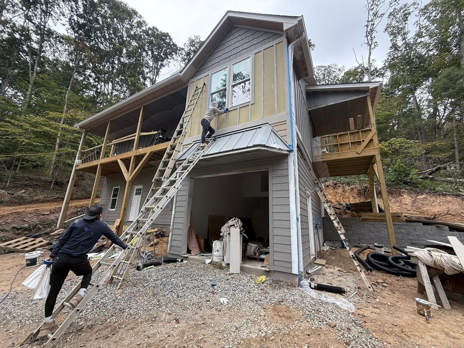 Gray two-story house under construction with exterior stairs, workers, and gravel yard