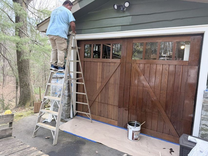 Person on ladder painting the trim above a brown garage door