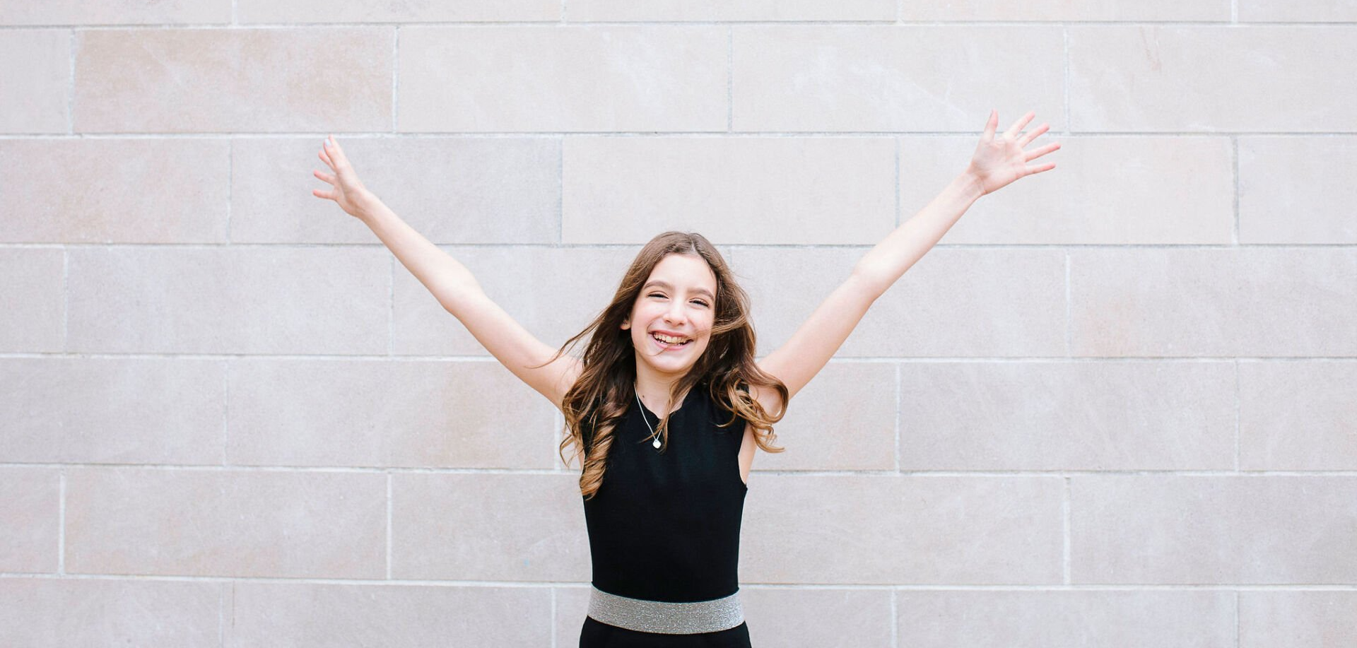 Happy girl throwing her arms up in the air before her bat mitzvah
