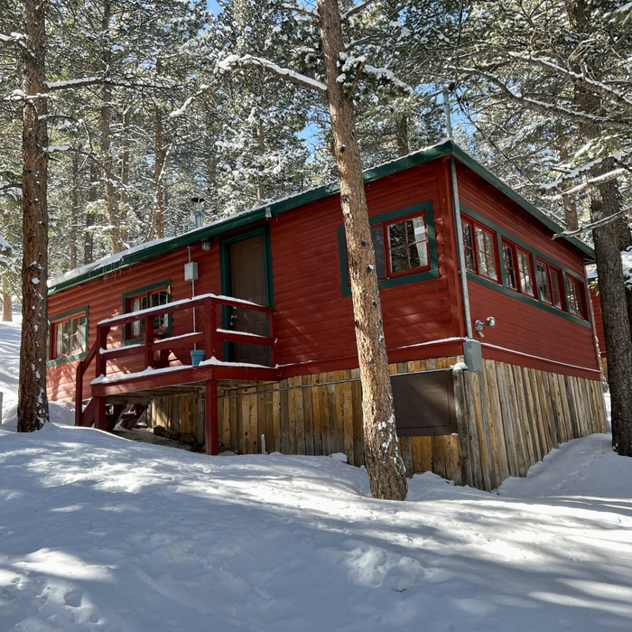 Red cabin in snowy pine forest with a small porch and red railing