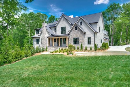 Large gray house with a steep roof, front porch, and green lawn under a blue sky