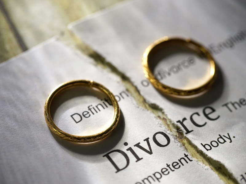 Two gold wedding rings on a divorce document, one resting on the word “Divorce”