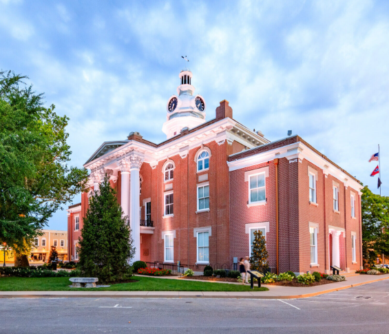 Historic red-brick courthouse with white columns and a domed cupola under a partly cloudy sky