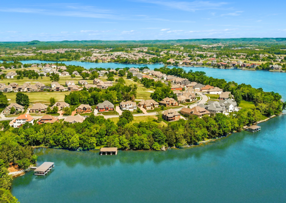 Aerial view of a suburban lakeside neighborhood with blue water, green trees, and houses along the shore