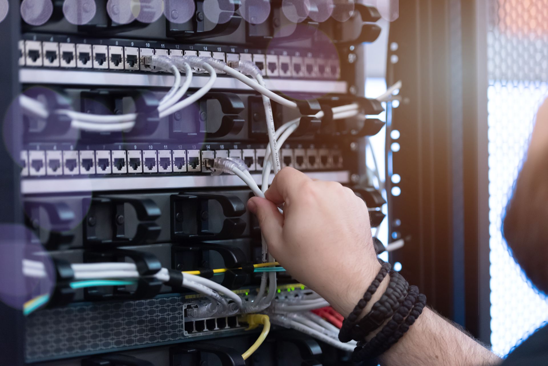 Person's hand adjusting network cables in a server rack, with various colored wires and connectors. Person's hand adjusting network cables in a server rack, with various colored wires and connectors.