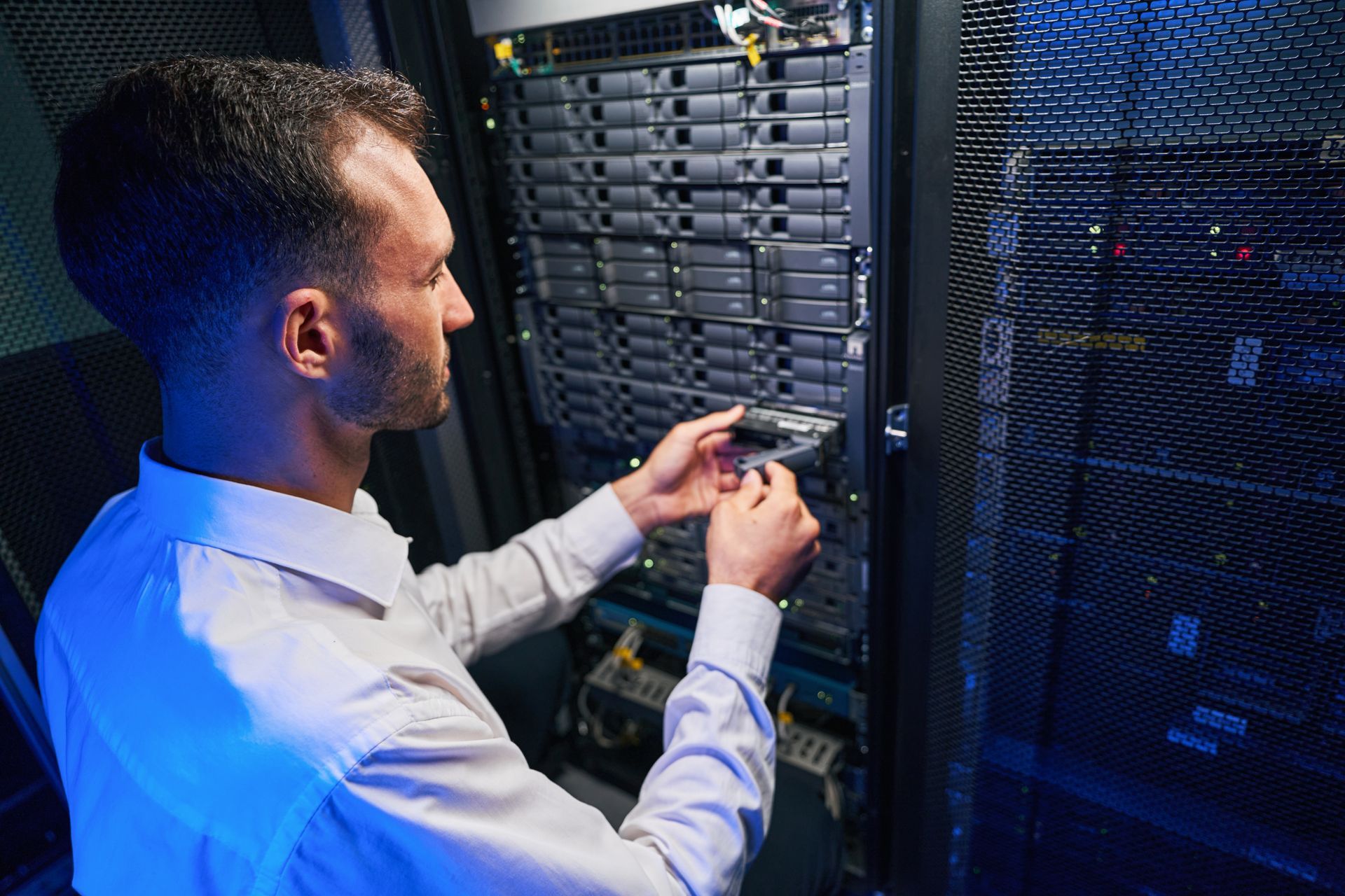 Man working on a server rack in a dark data center, holding a component. Man working on a server rack in a dark data center, holding a component.