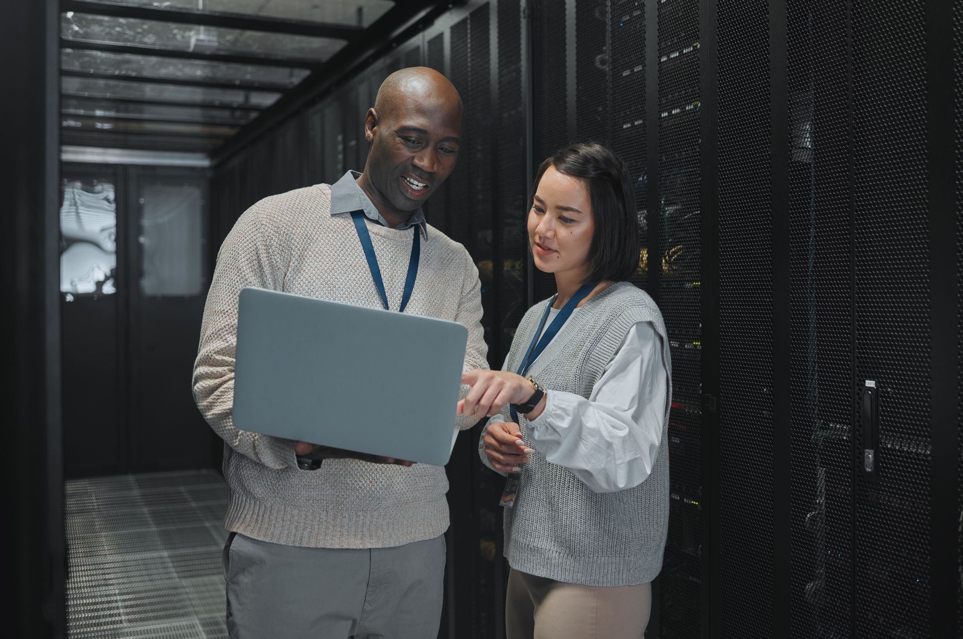 Two people in data center, looking at a laptop. The man points; woman watches. Servers in the background.