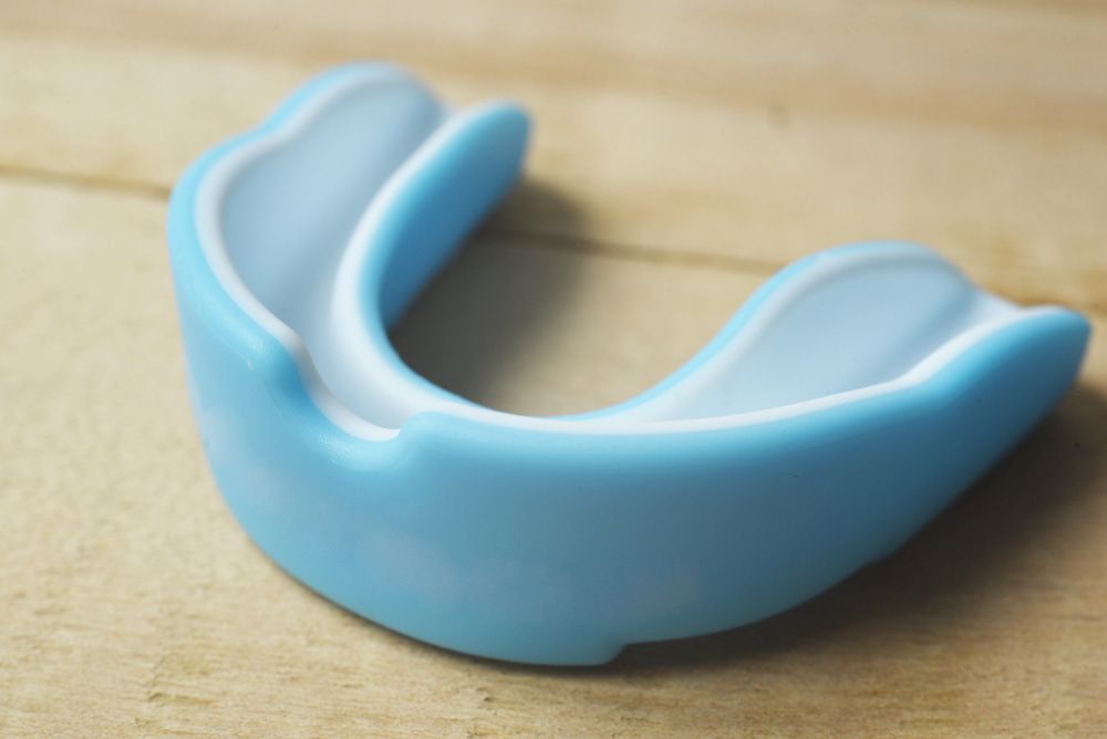 A Blue And White Mouth Guard Is Sitting On A Wooden Table — Highlands Denture Clinic in Willow Vale, NSW