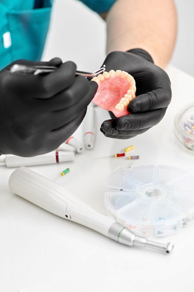 A Dentist Is Working On A Denture With A Pair Of Scissors — Highlands Denture Clinic in Willow Vale, NSW