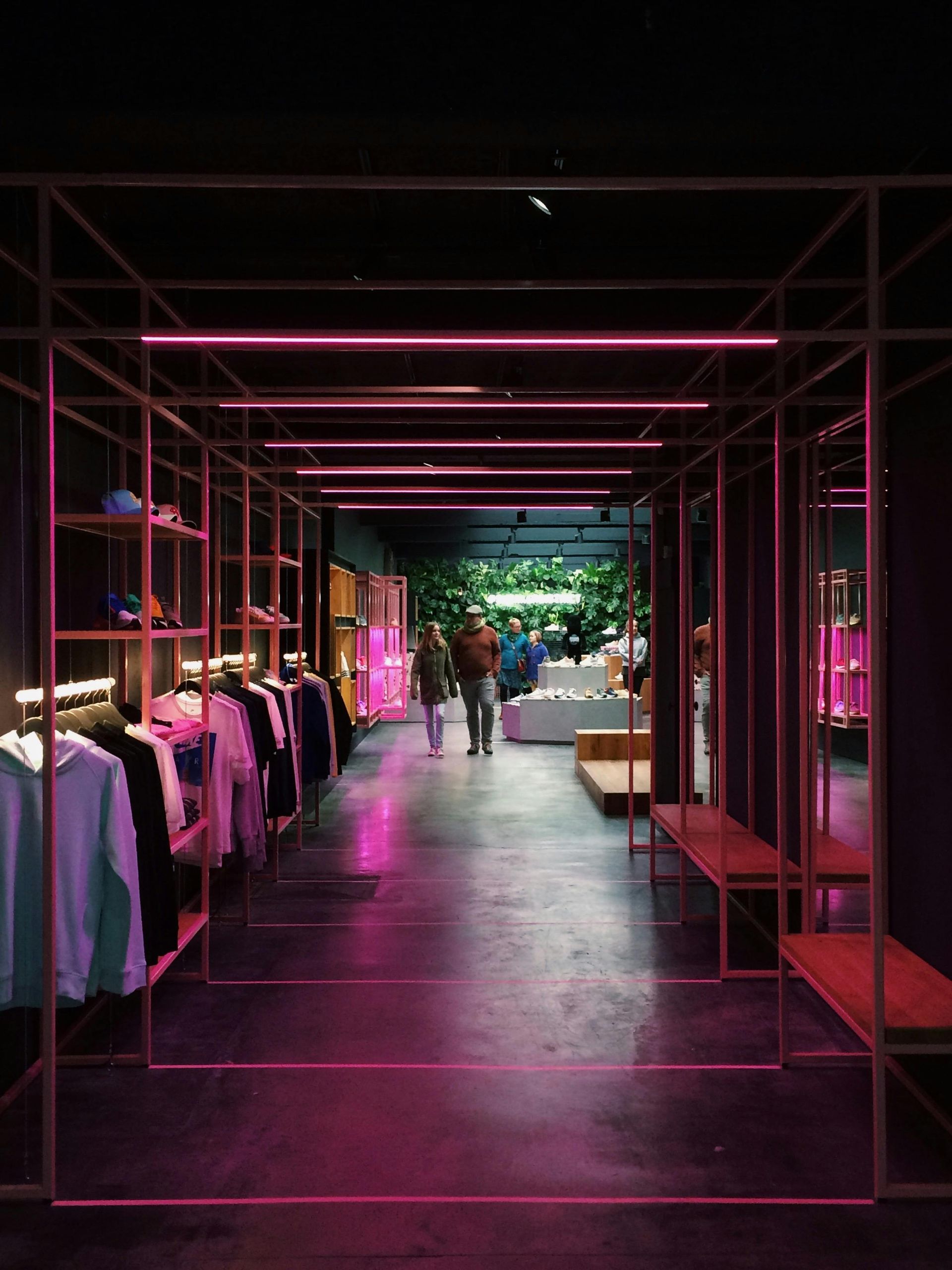 A retail space with pink neon lights, clothing racks, shelves, and a person walking down the aisle.