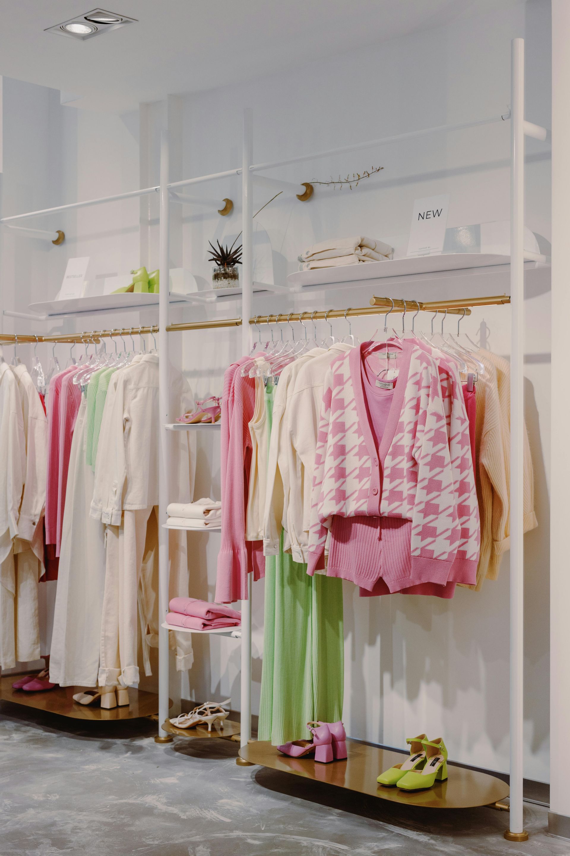 Clothing racks in a pastel-colored boutique. Dresses, sweaters, and shoes are arranged on shelves.