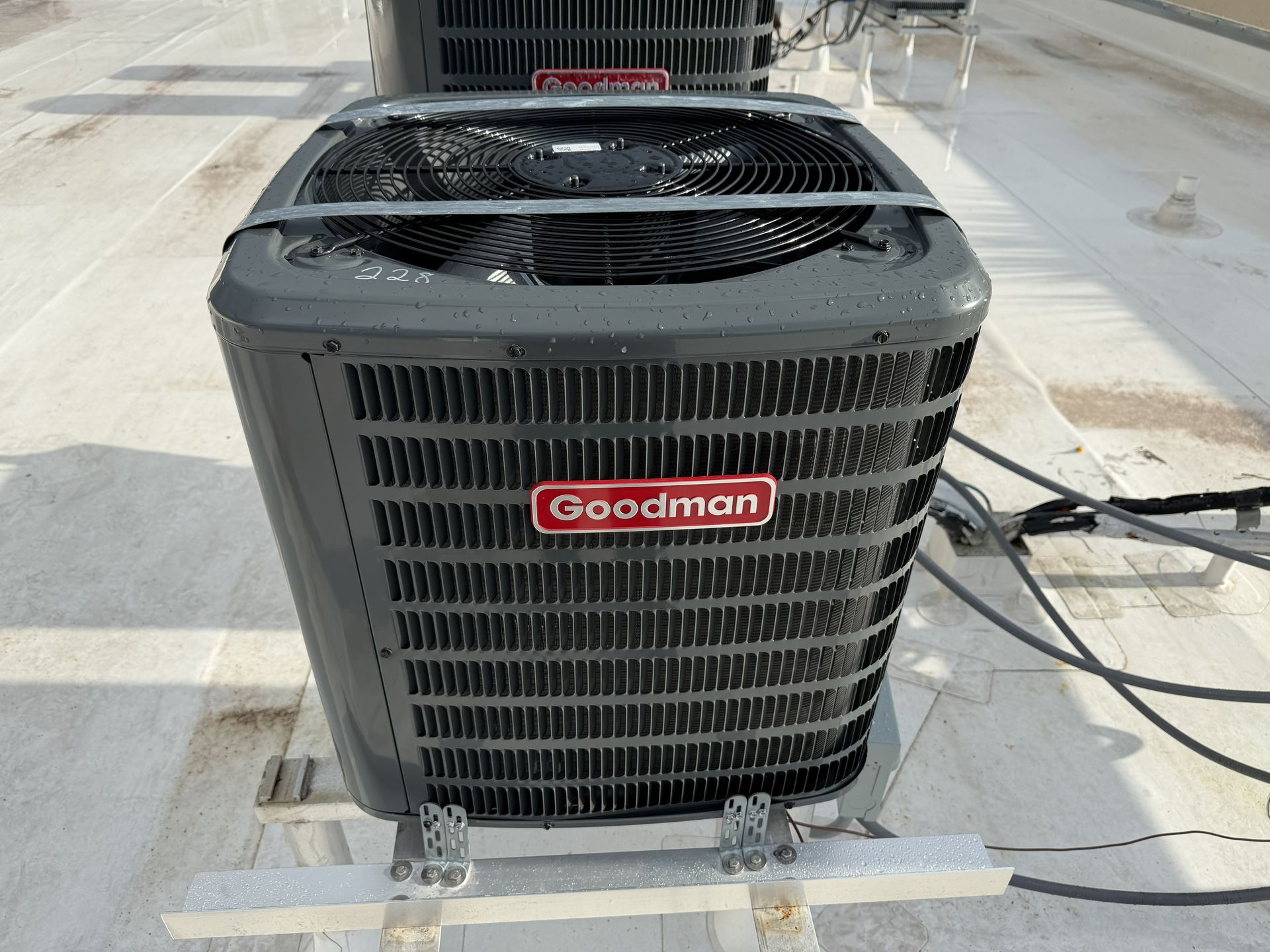 Goodman outdoor air conditioner unit on a concrete rooftop, with cables and another unit behind it