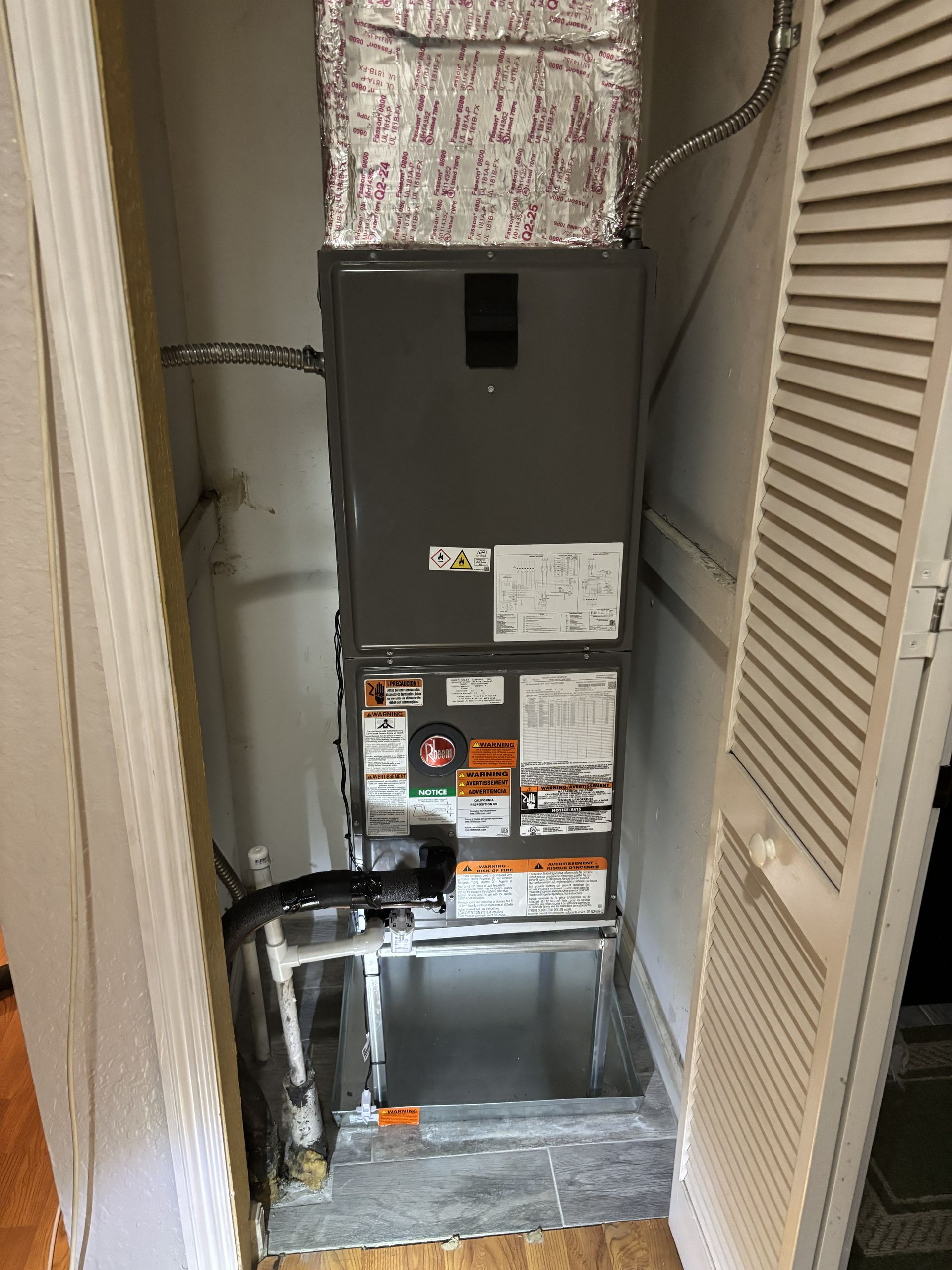 HVAC furnace and exposed ductwork in a narrow utility closet with open access panels.