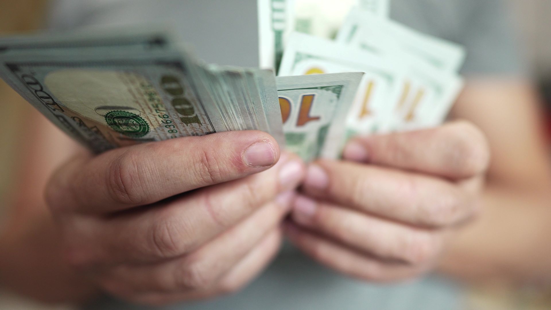 Hands holding and counting stacks of one-hundred dollar bills.