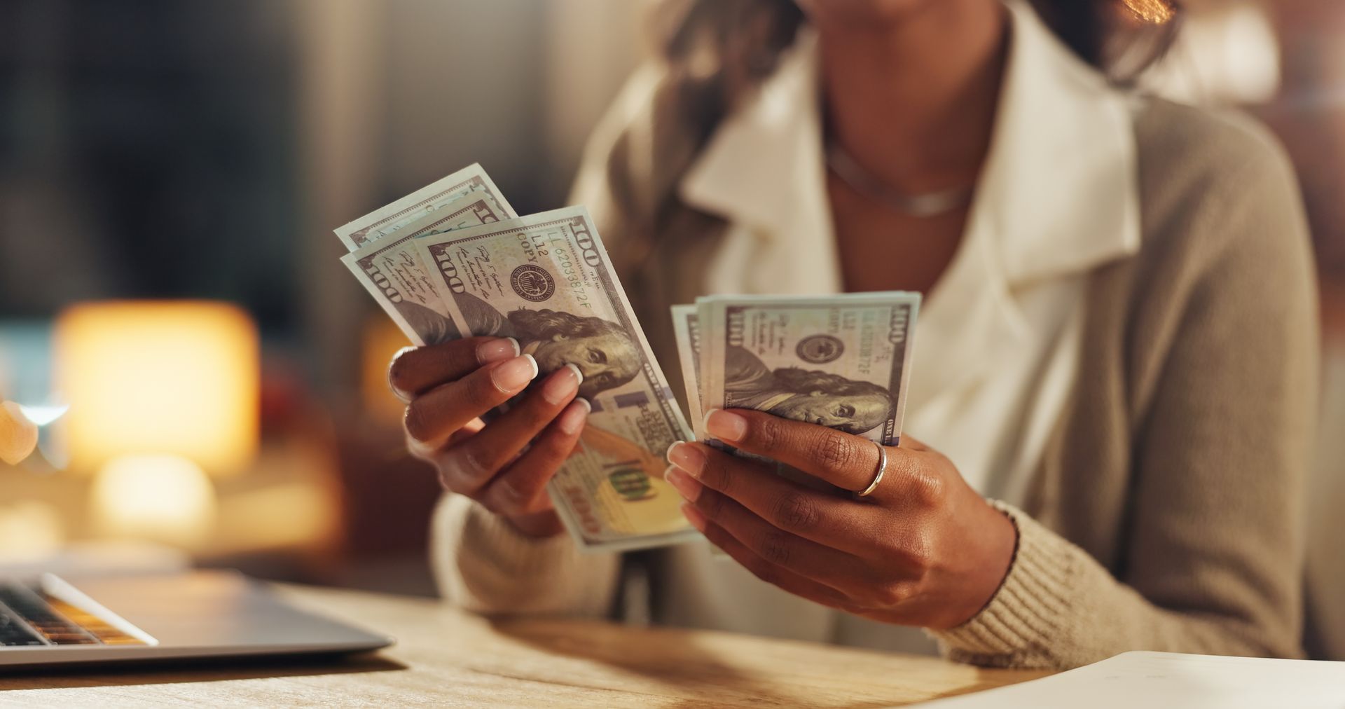 Person holding and counting stacks of US dollar bills.