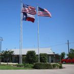 Flags of the U.S. and Texas waving in front of a building on a sunny day.