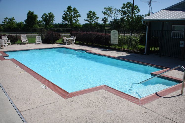 Pool with clear blue water and concrete surrounding, lounge chairs, and a small building in the background.