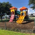 Playground with climbing wall, slides, and tunnel; enclosed by a fence.