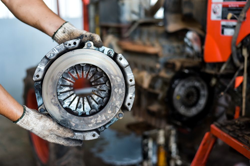A Man Is Holding a Clutch Cover in His Hands in Front of A Tractor — Leisure Coast Powder Coaters in Unanderra, NSW