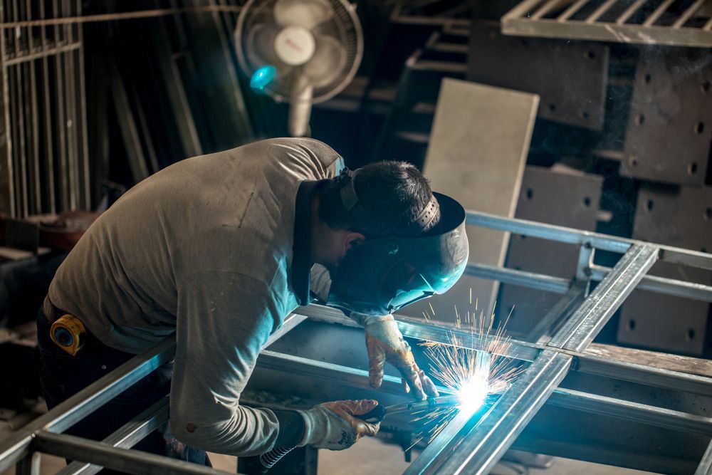 A Man Is Welding a Metal Frame in A Factory — Leisure Coast Powder Coaters in Wollongong, NSW