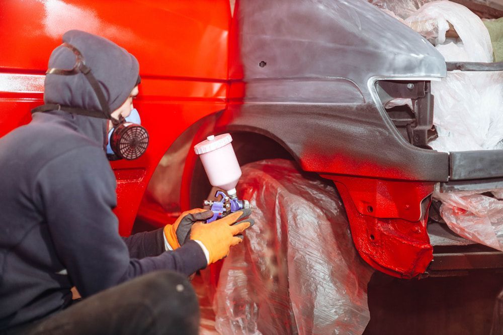 A Man Is Spray Painting a Red Car in A Garage — Leisure Coast Powder Coaters in Bowral, NSW