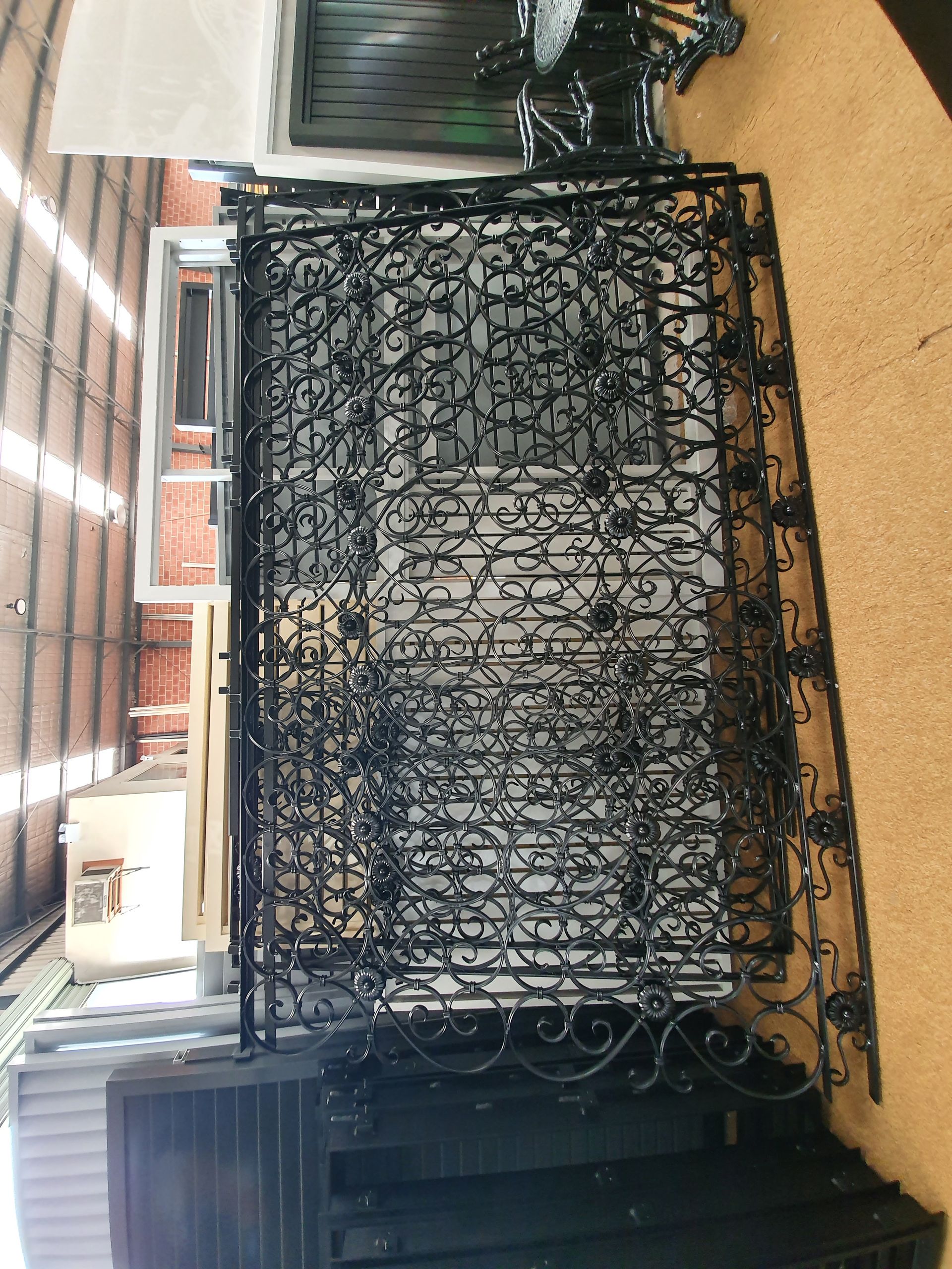 A Wrought Iron Fence with A Brick Wall in The Background — Leisure Coast Powder Coaters in Unanderra, NSW