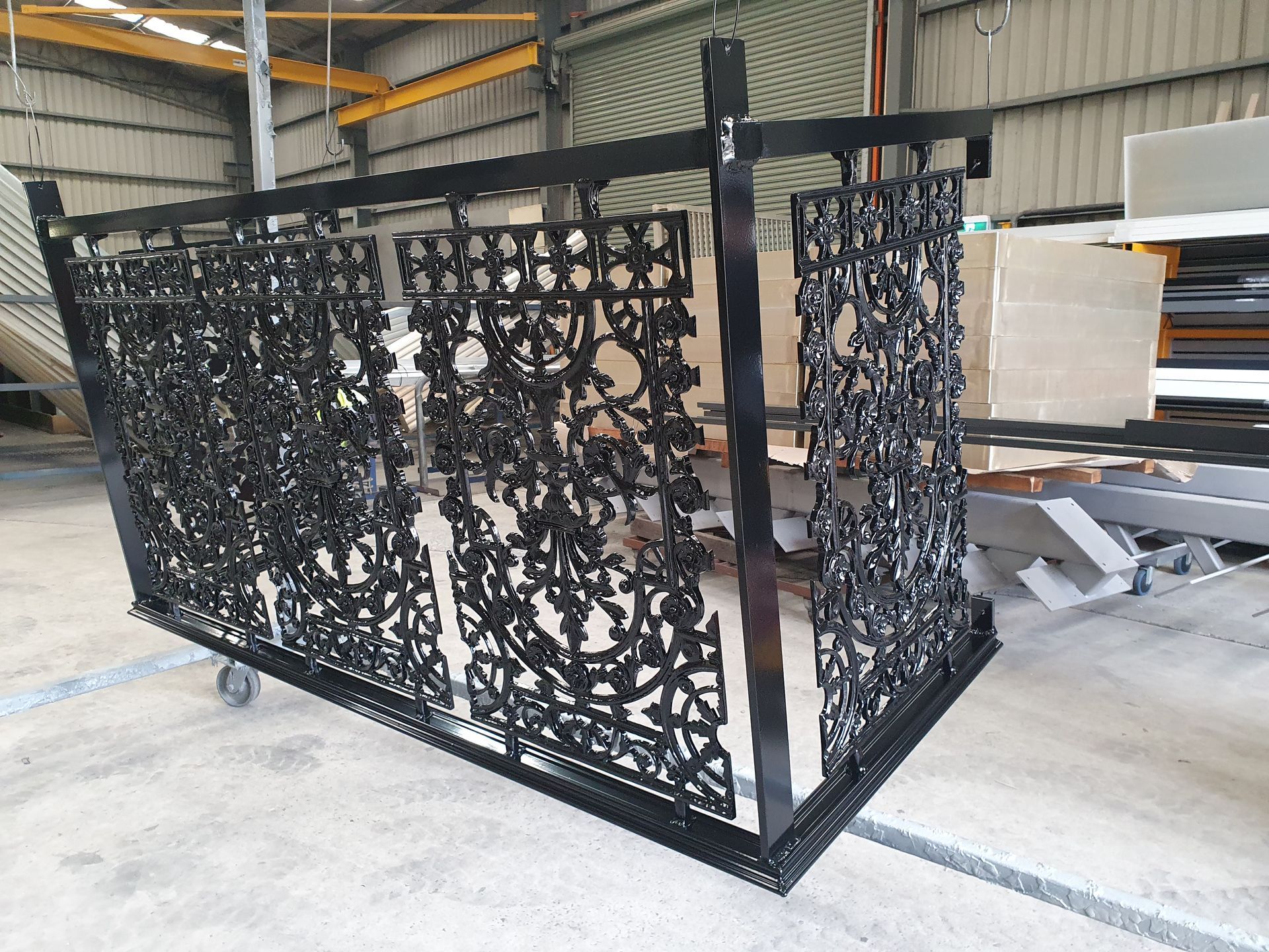 A Black Metal Railing Is Sitting on A Cart in A Warehouse — Leisure Coast Powder Coaters in Unanderra, NSW