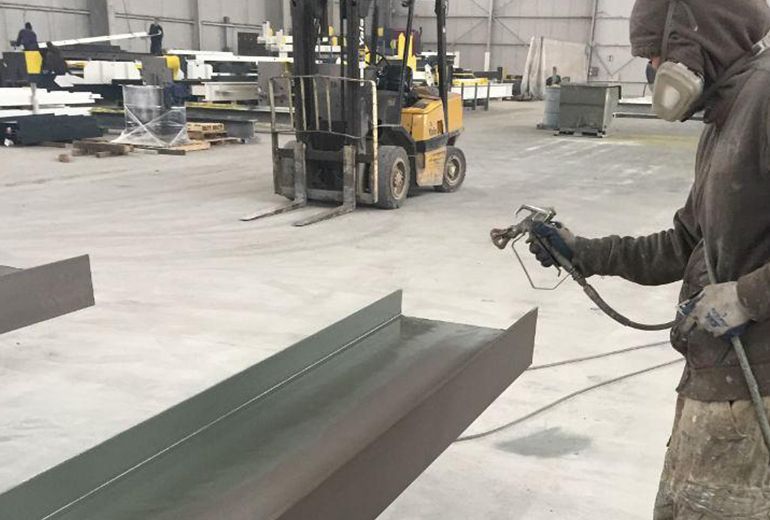 A Man Is Spray Painting a Piece of Metal in A Factory — Leisure Coast Powder Coaters in Unanderra, NSW