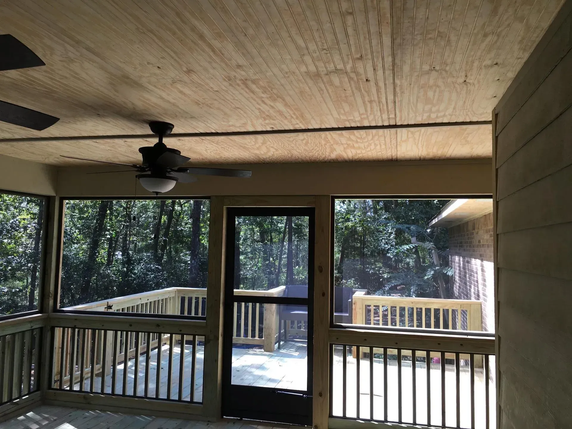 Screened porch with a ceiling fan, overlooking a wooded area.