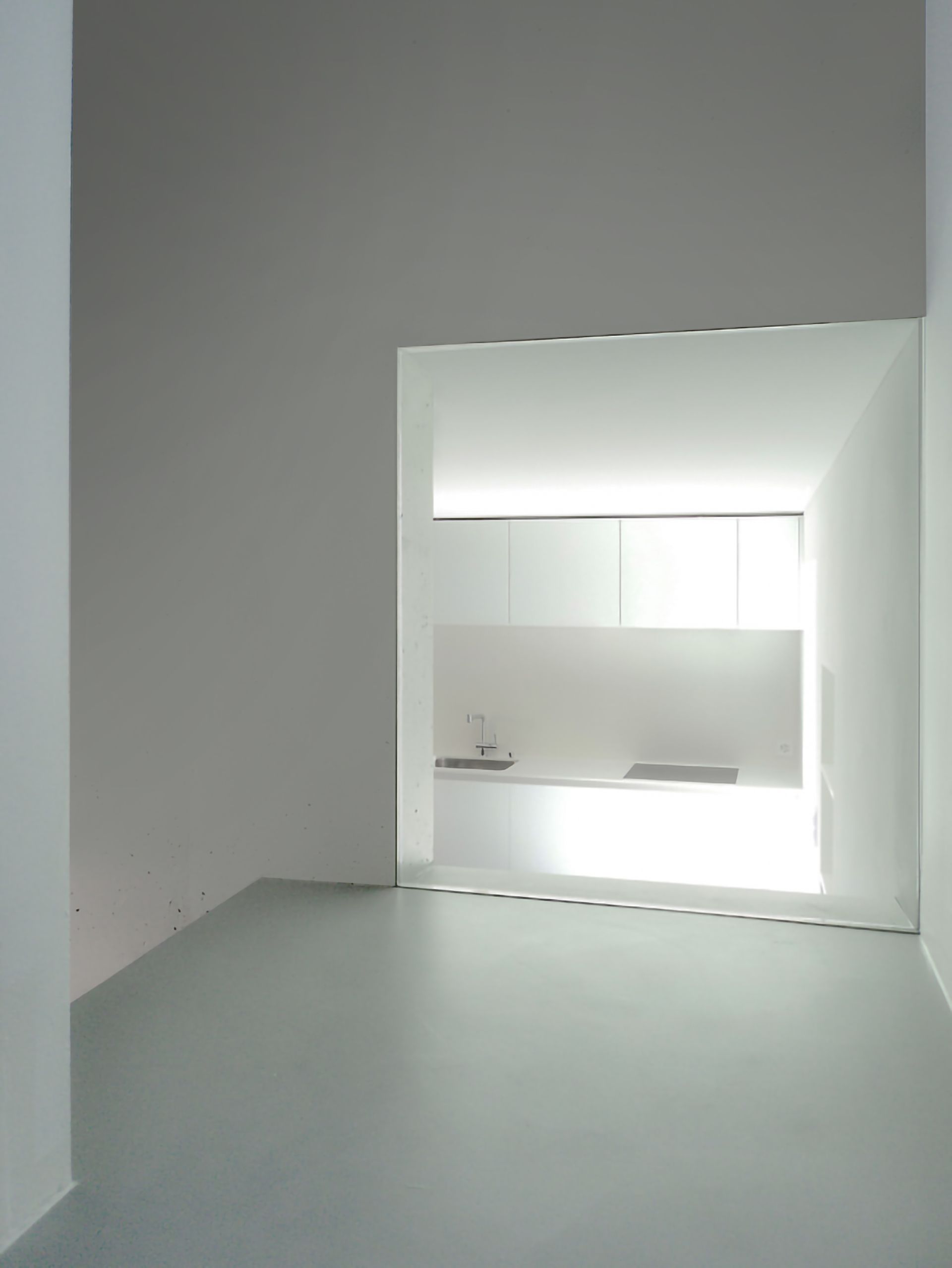 Stanza bianca, vuota e minimalista, con un'apertura luminosa sulla zona cucina.