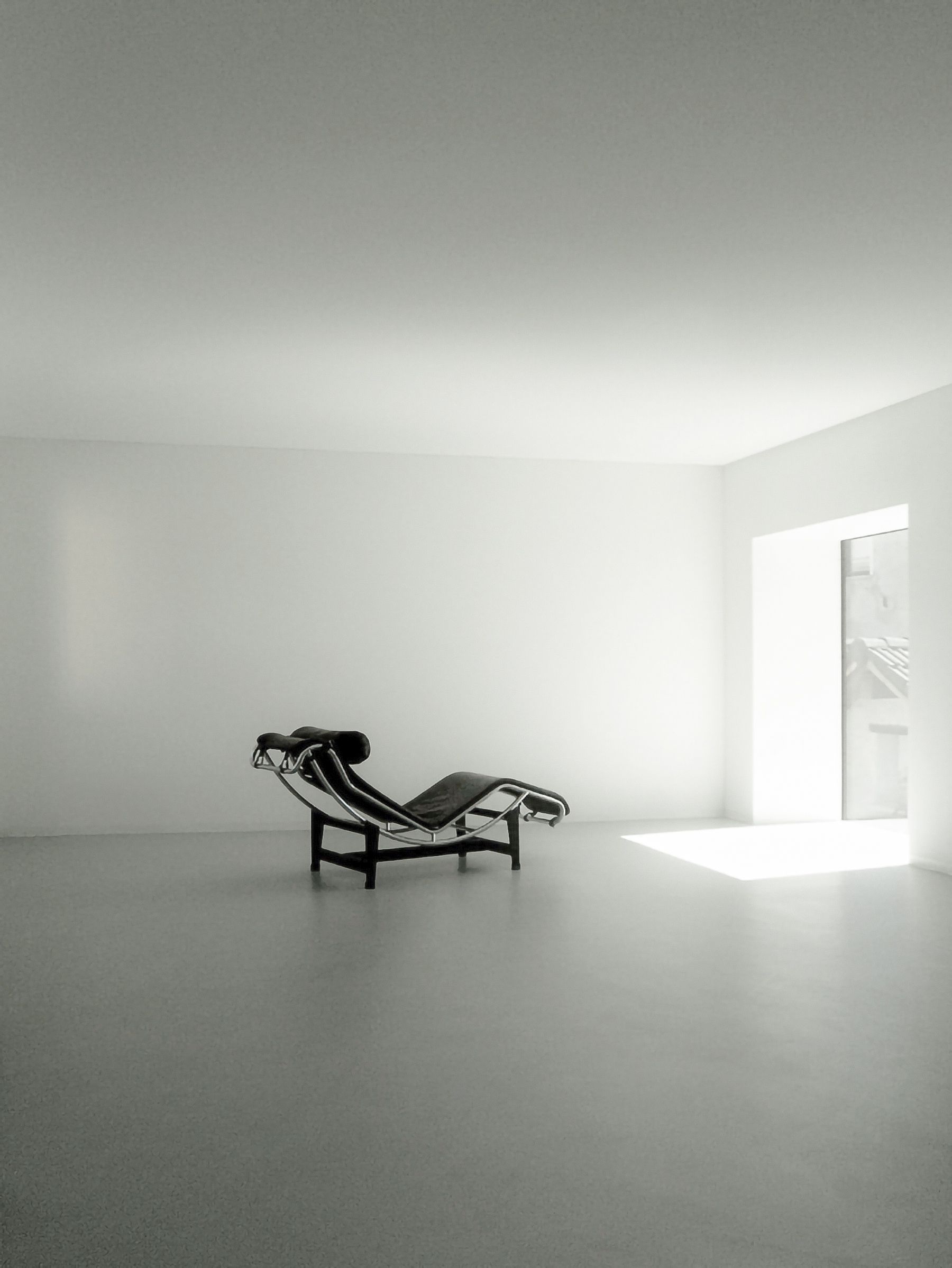 Stanza bianca minimalista con una chaise longue nera LC3 vicino a una finestra luminosa.
