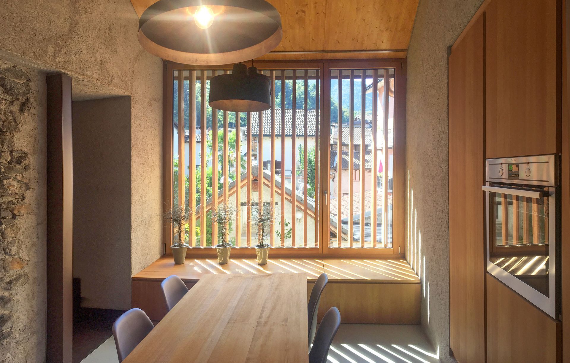 Zona pranzo interna con tavolo in legno, finestra a doghe e lampadari.