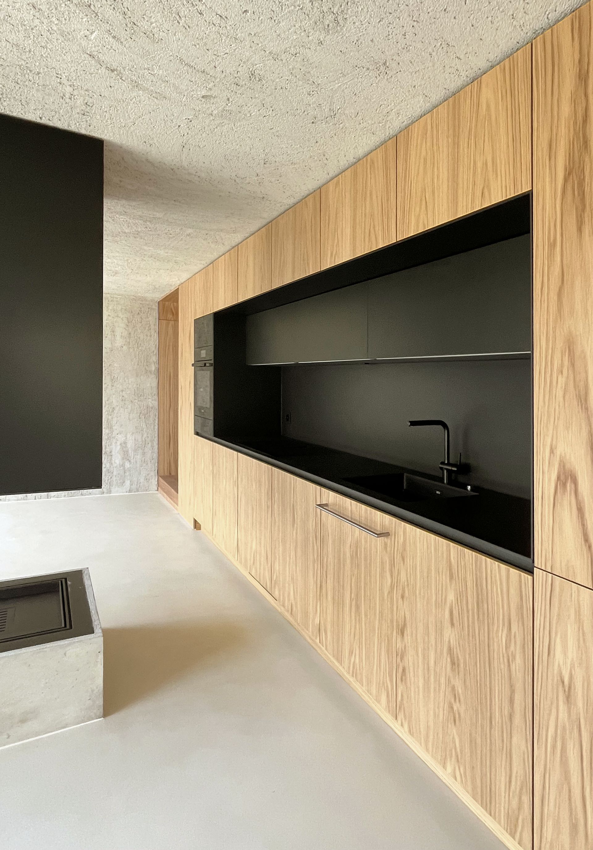 Cucina moderna con mobili in legno, piano di lavoro nero e zona cottura incassata.
