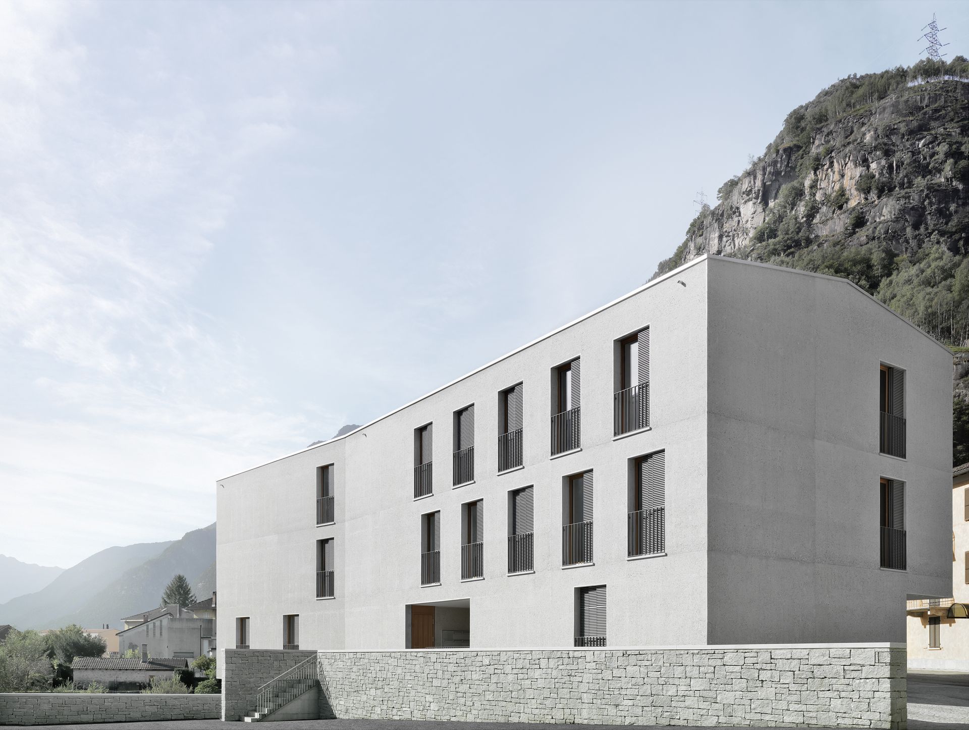 Edificio moderno, dai colori chiari, con finestre rettangolari e tetto piano, con sfondo montuoso.