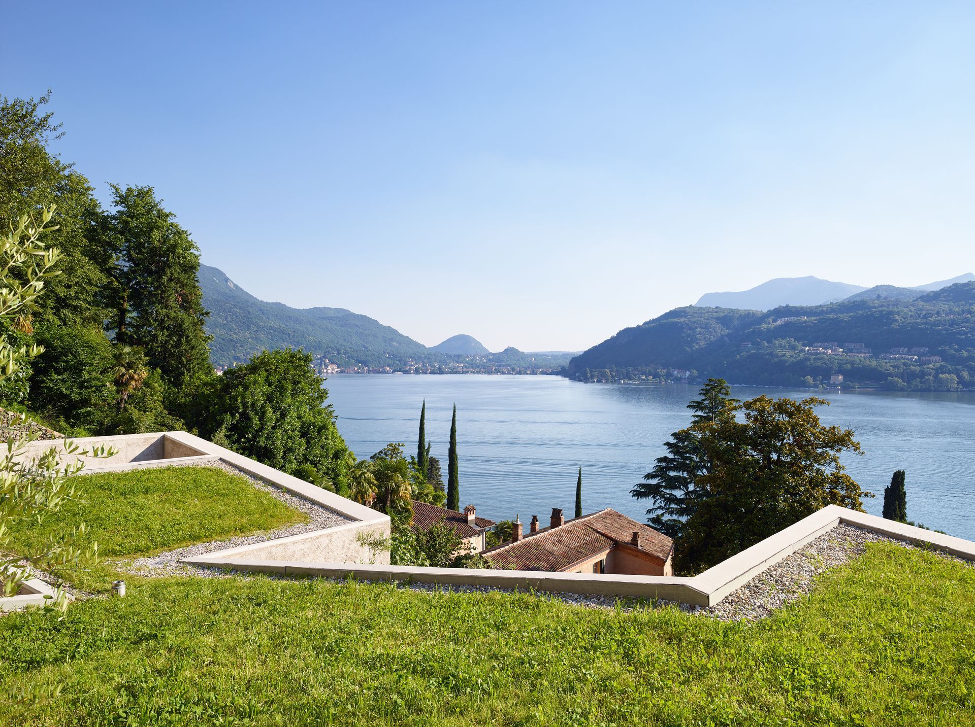 Vista panoramica di un lago circondato da montagne e vegetazione lussureggiante sotto un cielo azzurro e terso.
