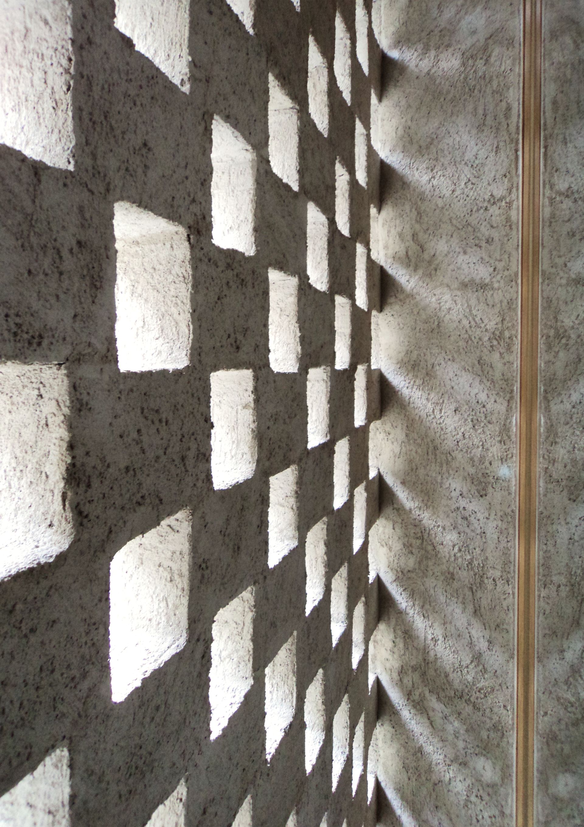Muro di blocchi di cemento con ritagli a forma di diamante che proiettano ombre modellate.