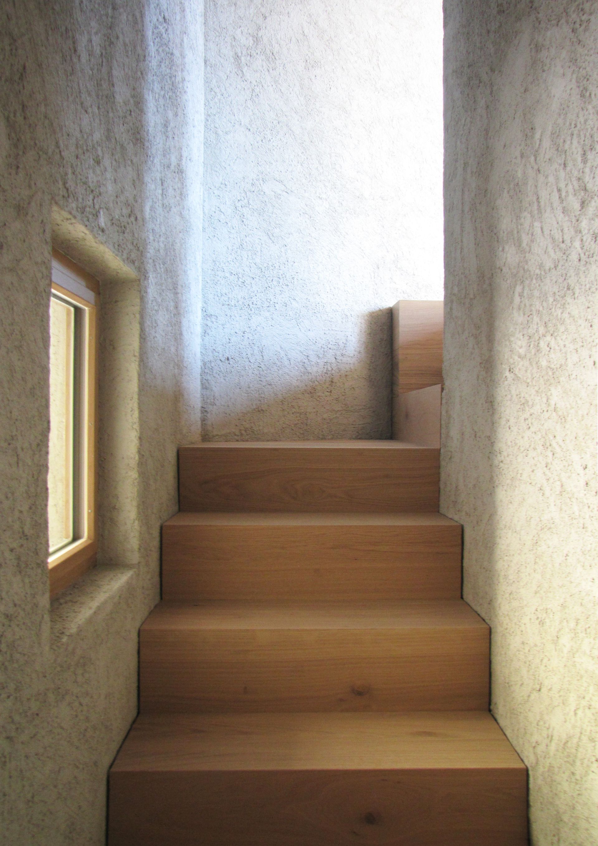 Scala in legno con una piccola finestra, incastonata in una parete con texture in pietra.