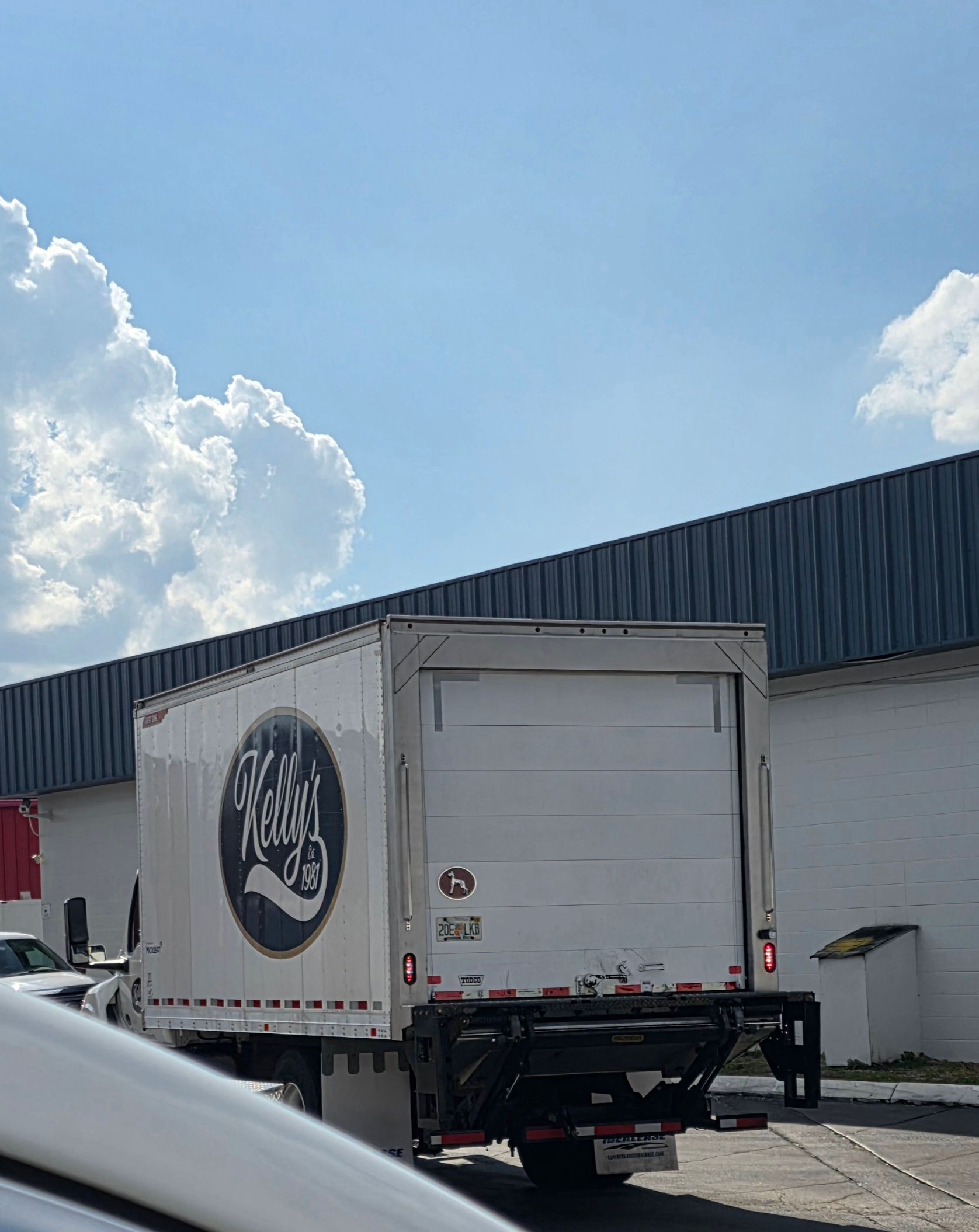 White box truck backed up to a warehouse loading dock under a bright blue sky.