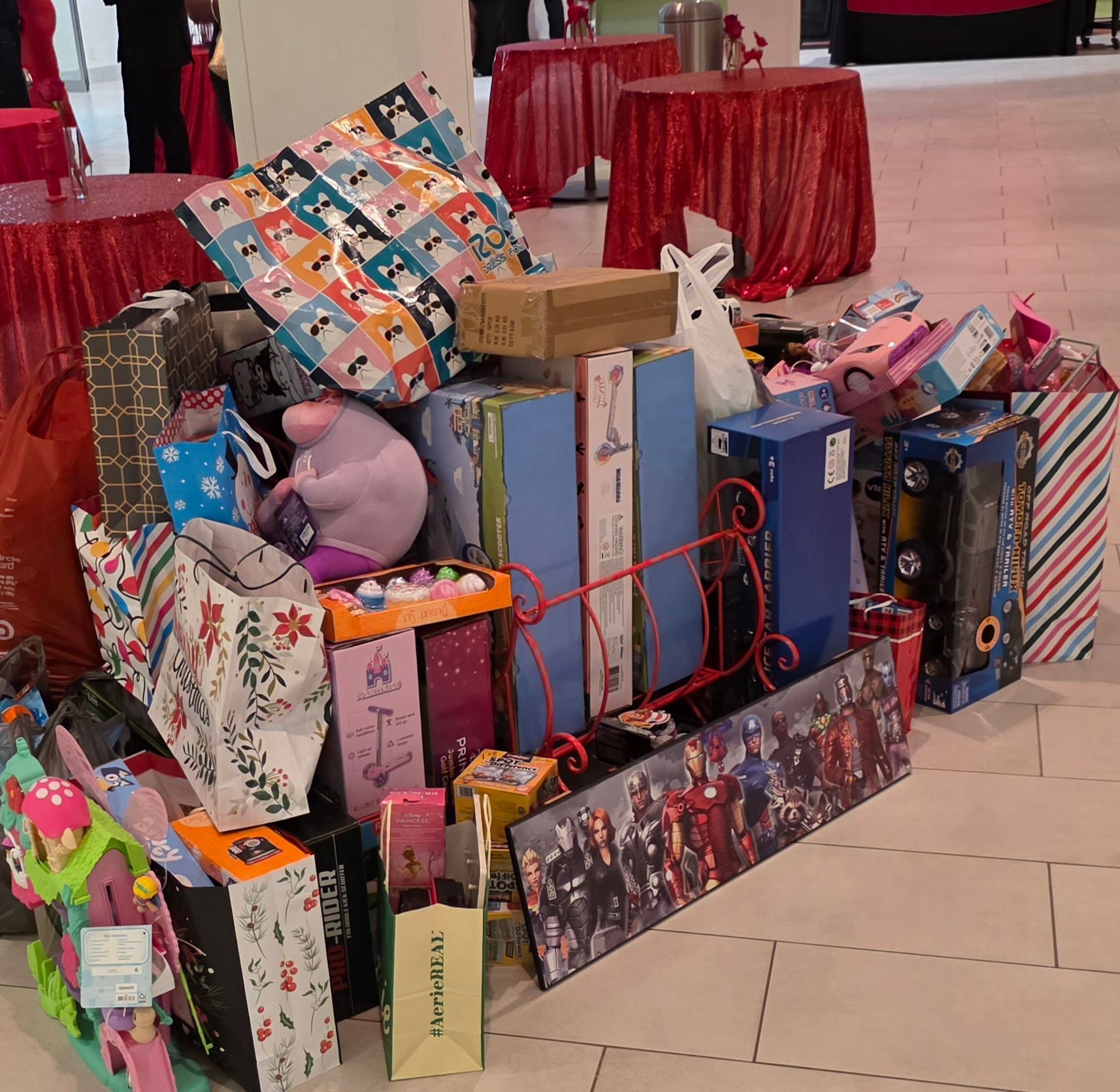 Pile of colorful wrapped gifts and boxes stacked on the floor at an indoor event.