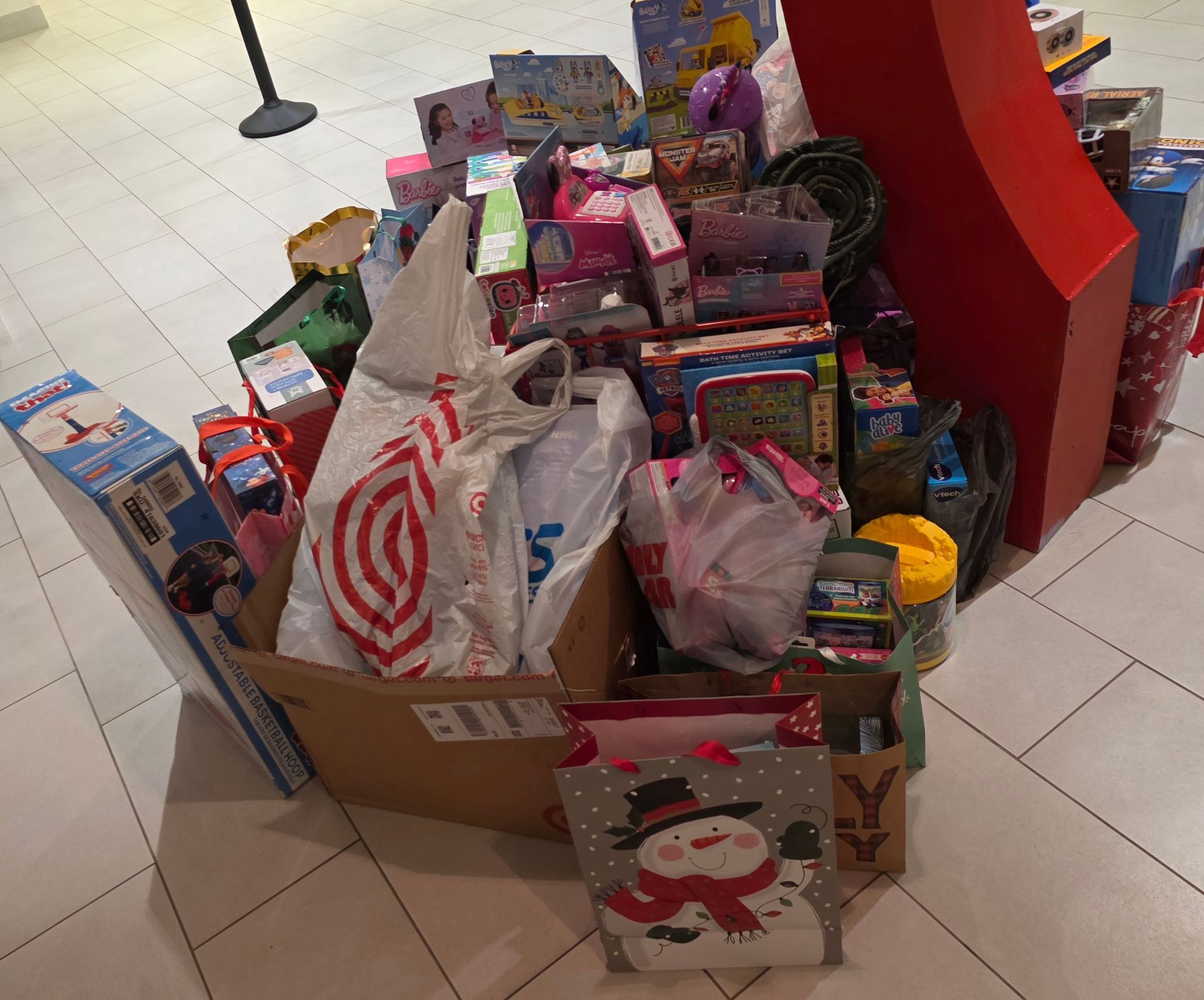 Donation box filled with wrapped gifts, toy boxes, and shopping bags in a store or mall.