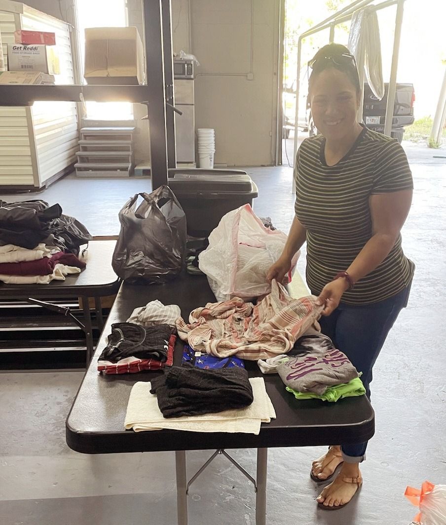 Woman organizing clothes on a table, preparing donations. Warehouse setting.