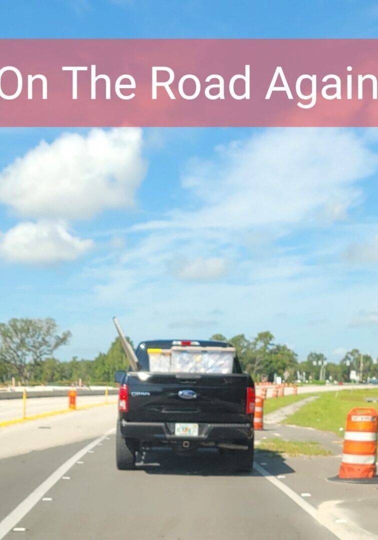 Black pickup truck on road with orange construction barrels, blue sky and text